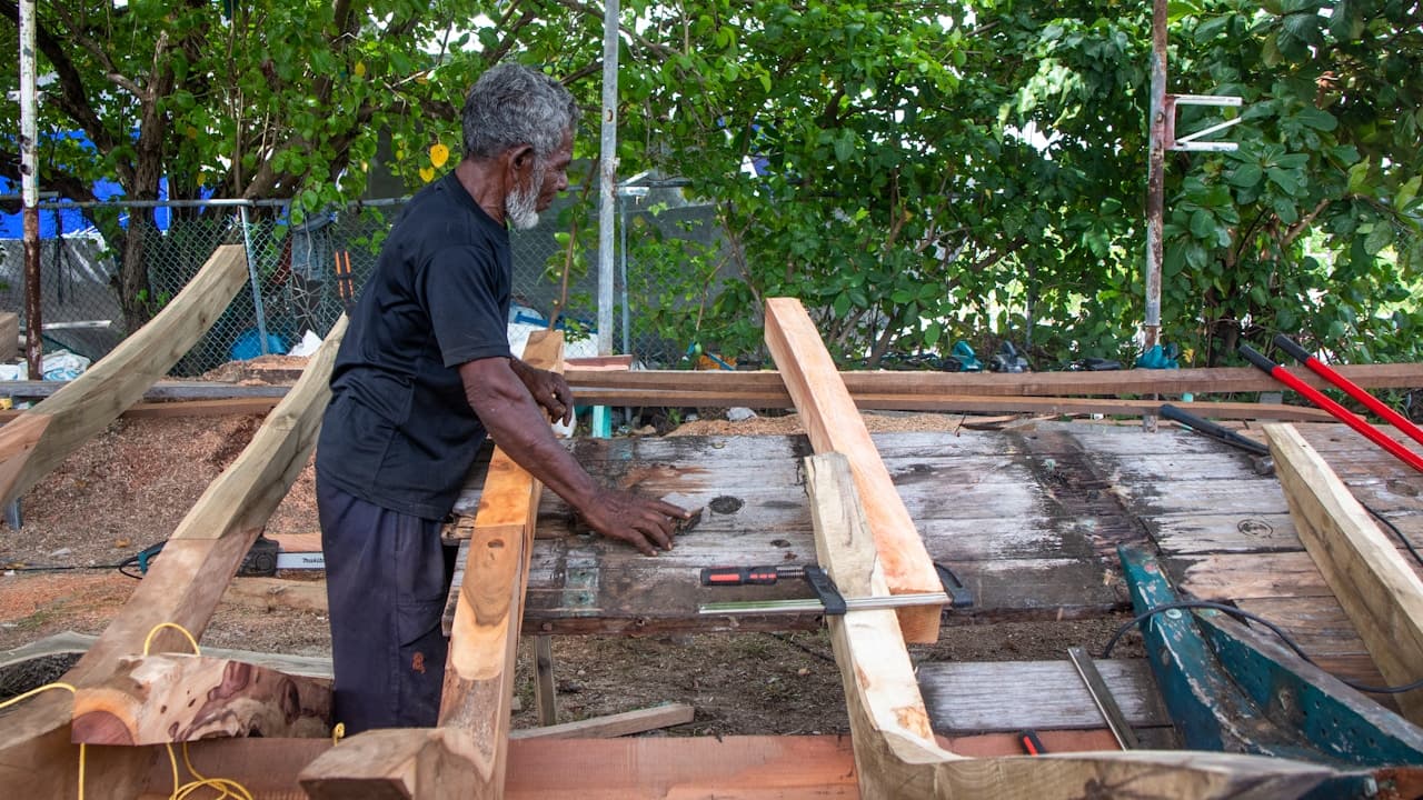 Artisan posant une lambourde en bois sur une structure de terrasse en cours de construction, avec niveau à bulle